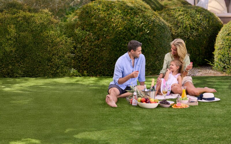 Rodina na pikniku na kvalitnom umelom trávniku v záhrade na jar, zelený trávnik bez blata a nerovností