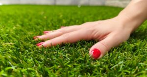 Ruka sa dotýka umelého trávnika naživo – detail hustých, jemných a realistických vlákien